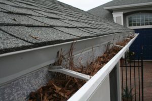 cleaning house gutter clogged with leaves is part of fall home maintenance